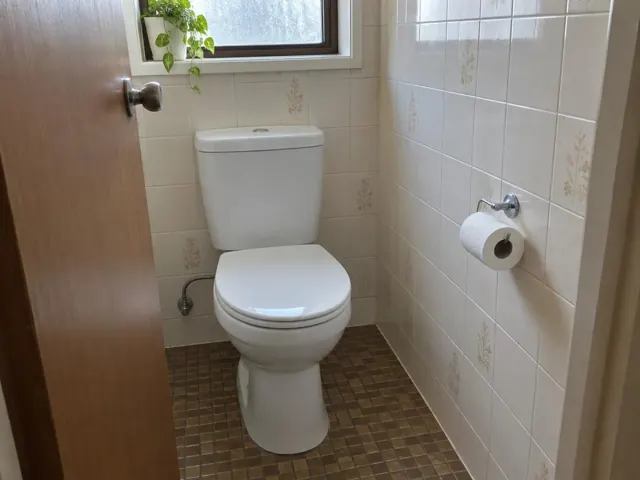 Clean white toilet in a small tiled bathroom with a window and towel holder in Kingsgrove