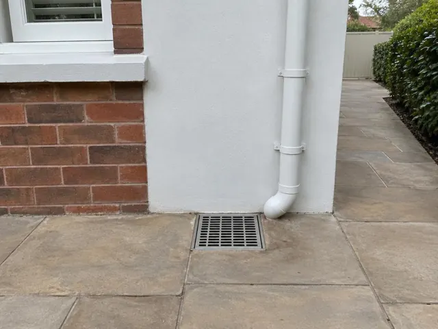 Outdoor grated gully beside brick and rendered wall with dry paved courtyard in Beverly Hills