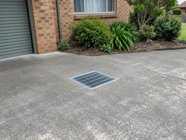 Flush driveway stormwater grate beside a brick house and garden in Bexley North